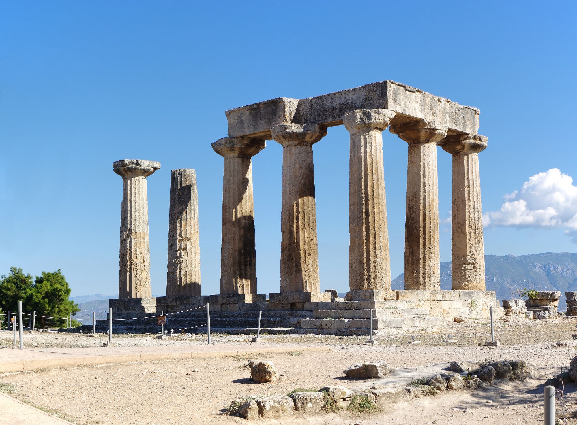 The Doric columns of the Temple of Apollo at Ancient Corinth against a deep blue sky