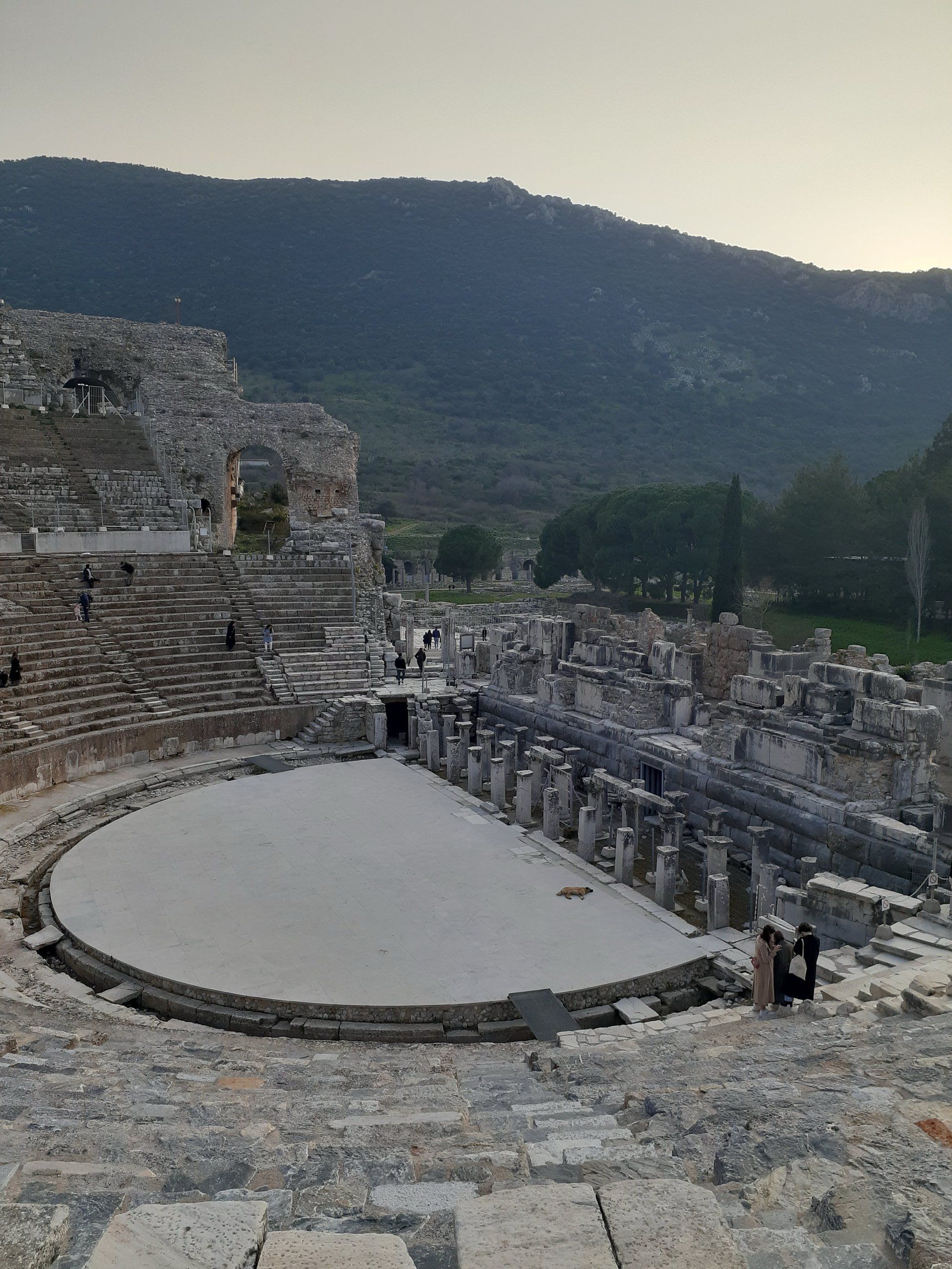 The Great Theatre of Ephesus at dusk, its marble stage circle and stone tiers seen from the upper seats