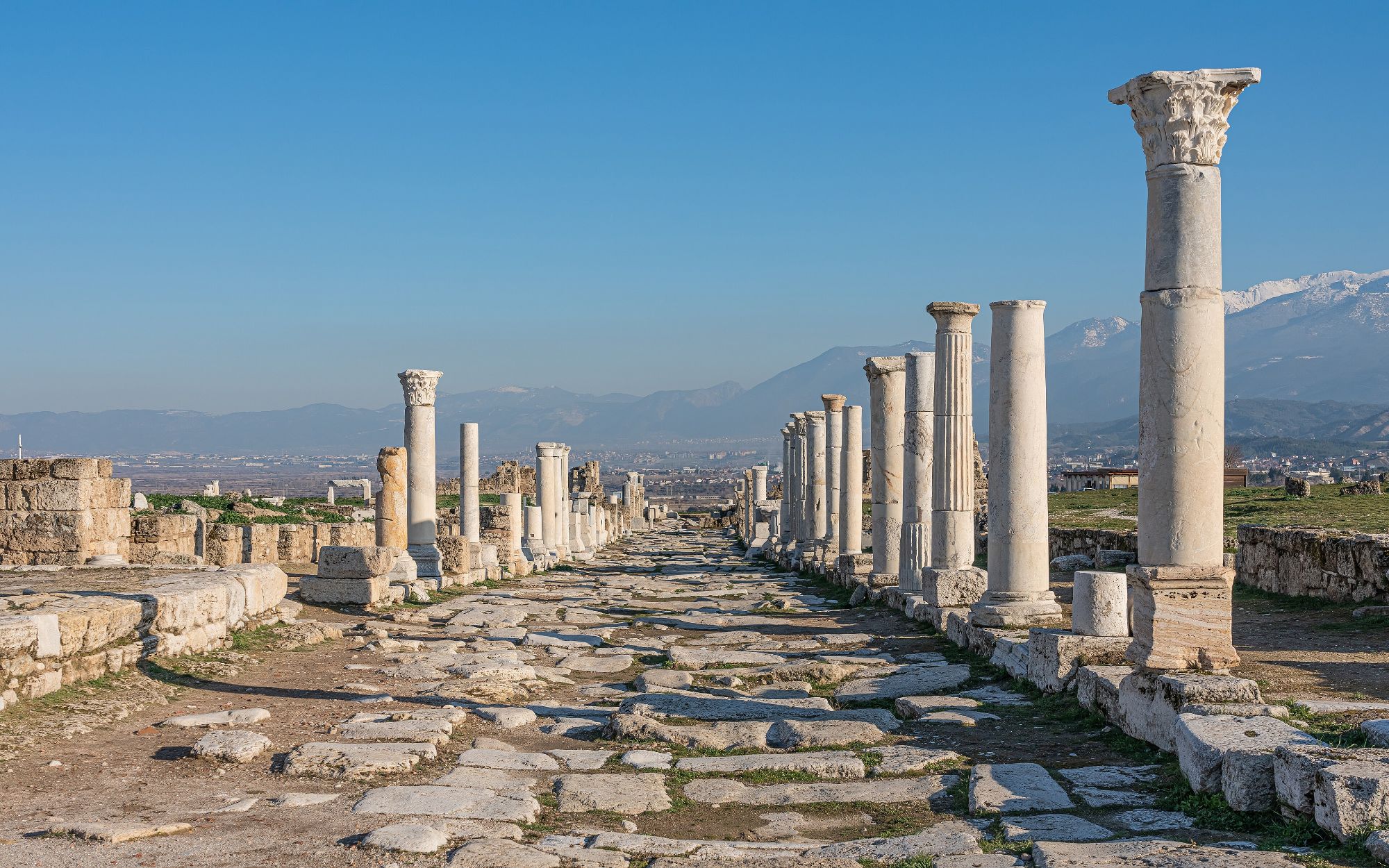The colonnaded main street of Laodicea, marble columns lining a Roman road with mountains beyond