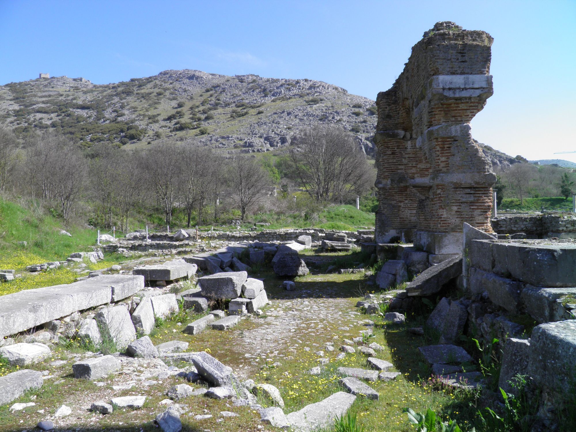 Fallen stones and the brick pier of Basilica B at Philippi, with the acropolis hill rising behind